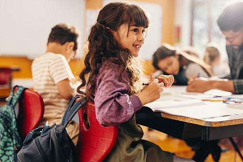 Education and child development. Little girl smiles while sitting in a class with her teacher and fellow students