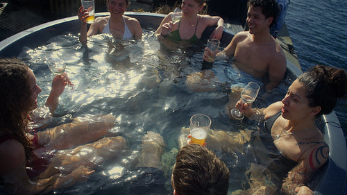 Friends relaxing in outdoor hot tub and toasting drinks by the waterfront