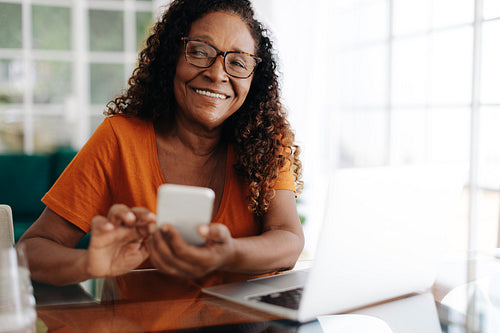 Happy mature woman using a mobile phone in her home office