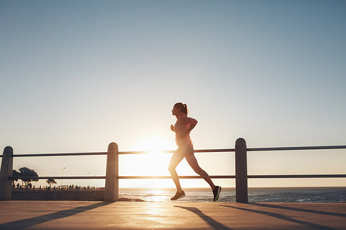 Young woman running along the sea during sunset