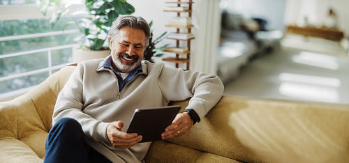 Bearded senior man views a tablet screen on the sofa