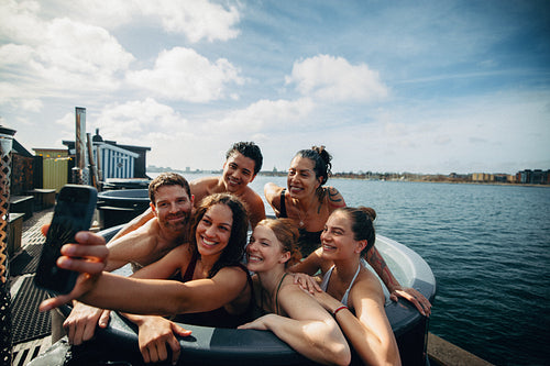 Friends taking selfie with phone in outdoor hot tub during happy vacation getaway