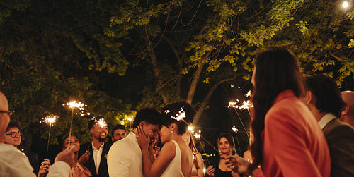 Outdoor wedding celebration with sparklers surrounded by friends in a romantic setting