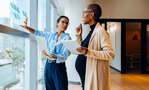 Two professional women discussing ideas and using technology in an office setting