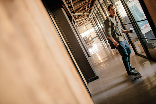 Handsome young man skateboarding in office corridor