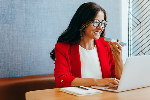 Woman in red blazer using phone for voice communication at a desk workspace