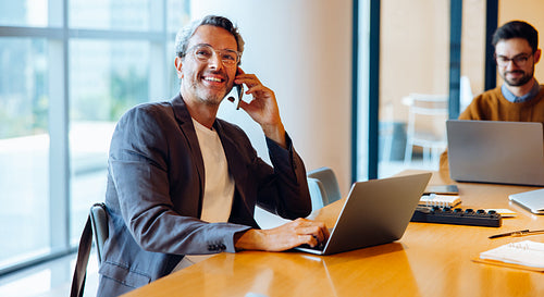 Confident professional man talking on the phone in office with laptop