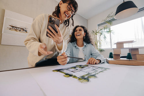 Two women collaborating in a bright office on architectural plans