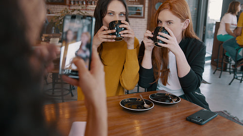 Woman taking photos of her friends drinking coffee at a cafe