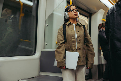 Commuter on subway wearing headphones and holding laptop