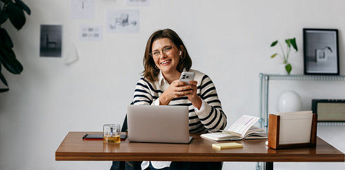 At the desk, the woman works with her laptop and phone in a styled office