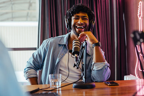 Joyful male podcaster laughing while recording a show in a studio with neon sign in the background