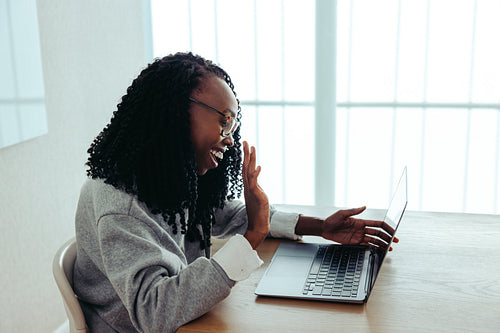 Smiling black businesswoman waving during video call on laptop in bright office space