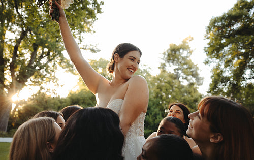 Joyful bride getting lifted by her close friends outdoors during golden hour celebration