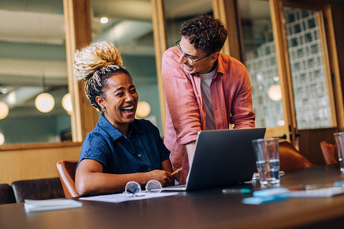 Two colleagues laughing together while working on a project at the office