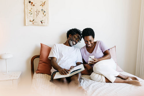 Couple relaxing in bed enjoying leisure time together with books and technology