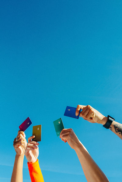 Young adults display colorful credit cards under a clear blue sky
