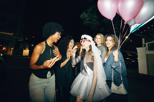 Group of young friends celebrating a bachelorette party at night with balloons