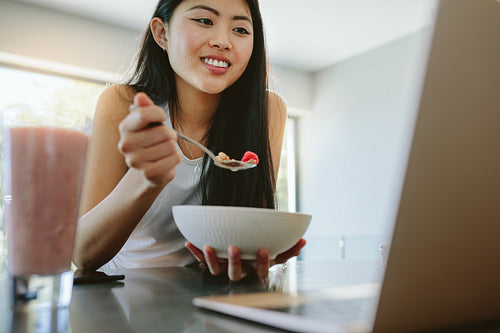 Woman having breakfast and using laptop