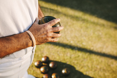 Close up of a man standing in a lawn holding a boules