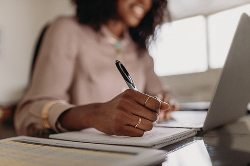 Woman making notes looking at laptop working from home