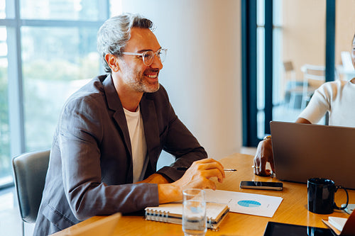 Man smiling at a meeting with documents and laptops on the table