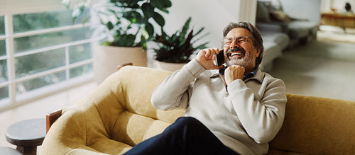 Senior man laughs while talking on smartphone at home