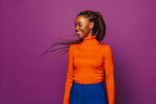 Confident young woman with vibrant two-tone braids smiling against purple background