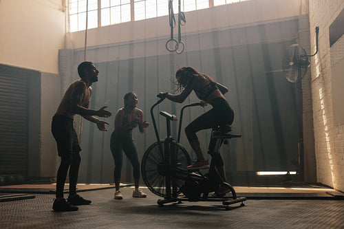 Friends motivating woman on exercise bike in gym