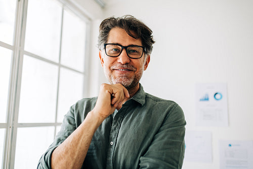 Senior business man stands in an office looking at the camera