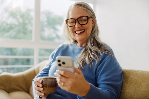 Grey-haired senior checks a smartphone on a sofa