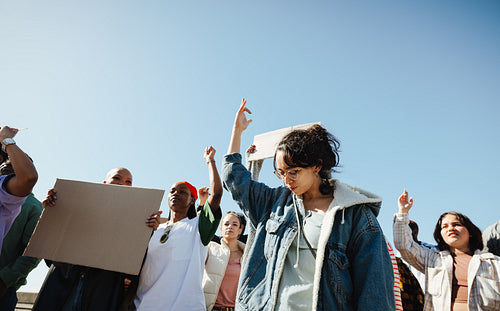 Group of diverse individuals demonstrating with raised hands outdoors