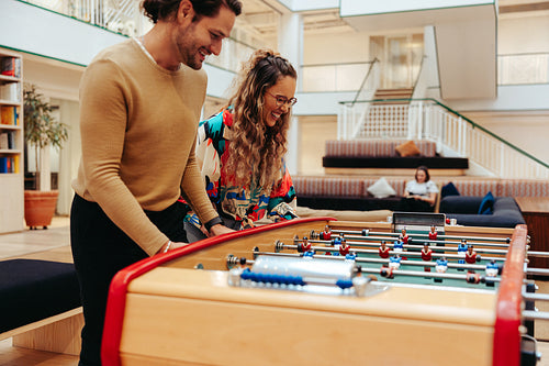 Coworkers enjoying a fun and relaxing lunch break playing foosball in a modern office