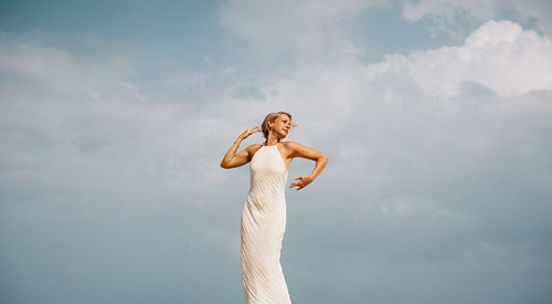 Elegant woman in white dress posing gracefully under a cloudy sky