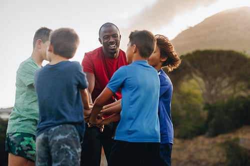 Rugby coach and his students putting their hands together in a huddle