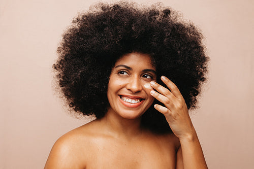 Beautiful woman with Afro hair applying cosmetic moisturizer on her face