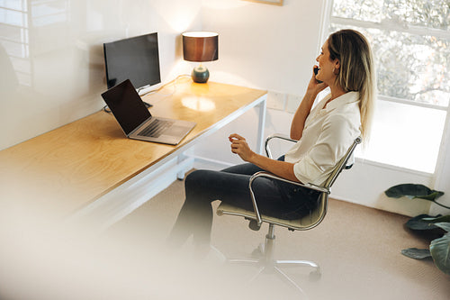 Happy young businesswoman having a phone call in her office