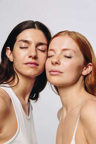 Two women with glowing skin pose peacefully in studio
