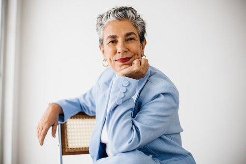 Elegant female professional sitting on a chair, dressed in a sharp office suit and grey hair