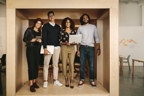 Happy teammates standing in office with laptops and tablet. 