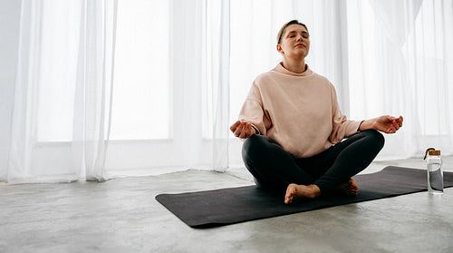 Woman practicing yoga meditation at home on mat in bright indoor wellness routine