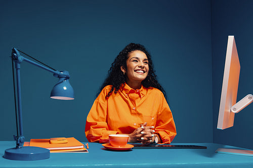 Young woman sitting with hands clasped and smiling in a monochromatic office