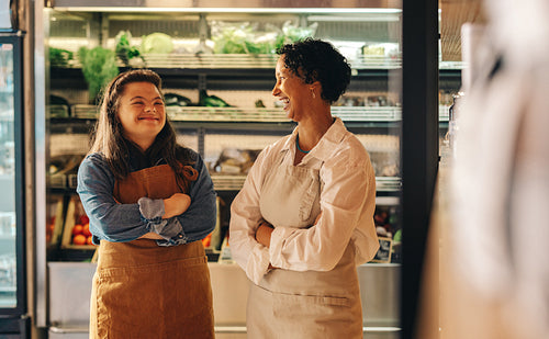 Two grocery store workers laughing cheerfully in their shop