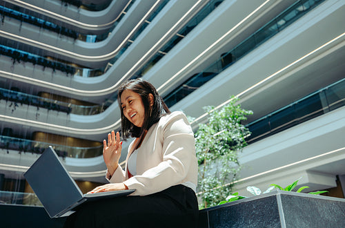 Professional woman waving during a virtual meeting outside office