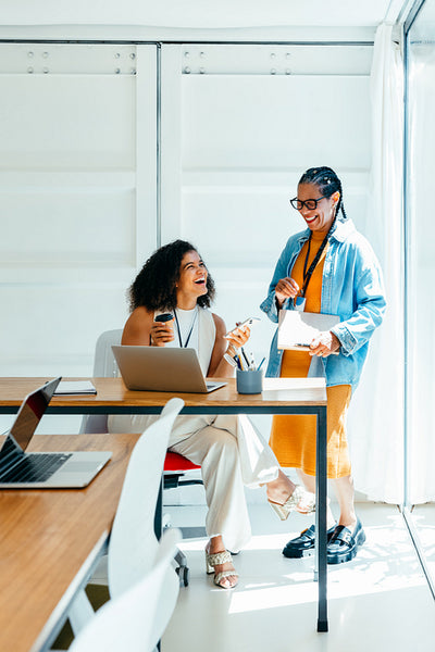 Cheerful coworkers collaborating in a state-of-the-art office space with laptops, enjoying a positive work atmosphere and vibrant discussion by the window