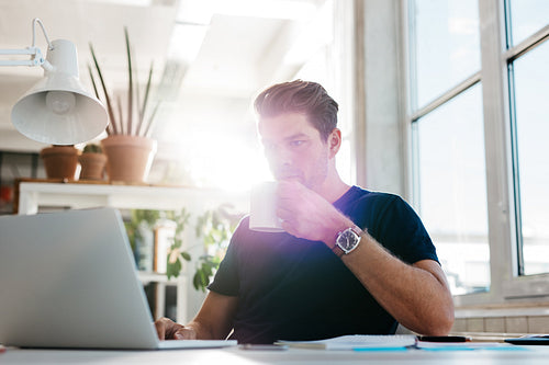 Young businessman drinking coffee and looking at laptop