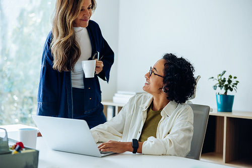 Two women coworkers chat near laptop at office