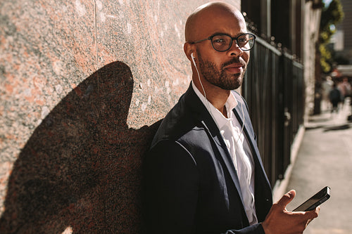 Handsome businessman with phone leaning on a wall outside