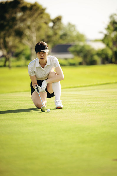 Focused woman golfer crouching for precision on golf course on the putting green