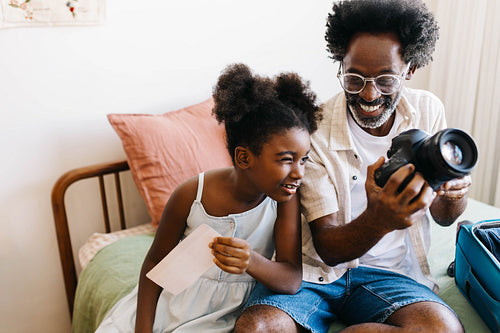 Family vacation: Father shows his daughter how to use a travel camera while packing